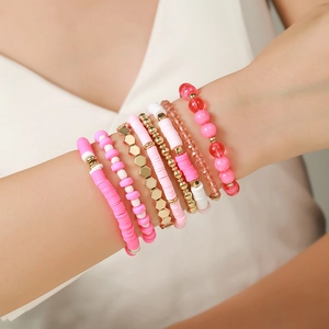 Detail of layered bohemian bracelets with pink and white clay beads and gold accents
