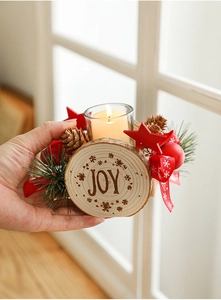 Close-up of wooden Christmas candle holder featuring JOY engraving and pine cone detail