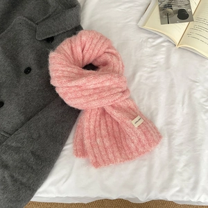 Close-up of pink knit wool scarf texture with brand label on a soft fabric surface