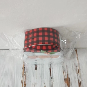Detail of Santa Claus tin box with red and black plaid lid on a white wood surface