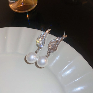 Macro detail of silver wing earrings with sparkling rhinestones and elegant white pearls