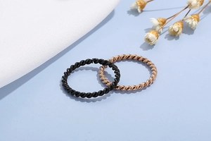 Detail of twisted rope rings in black and rose gold finish on a soft blue background