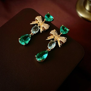 Détail de boucles d'oreilles vintage avec nœud doré et zircons vert émeraude