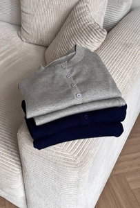 Detail of soft knit cardigans in grey and navy blue neatly folded on a corduroy sofa