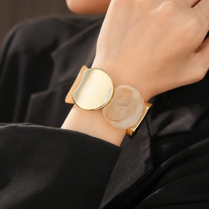 Macro view of wide gold metal and marble resin textured panels on the elastic bracelet