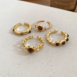 Macro detail of four gold-plated tiger eye rings showing varied textures and stone settings