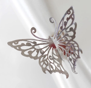 Close-up of silver butterfly napkin ring with laser-cut hollow design on white fabric