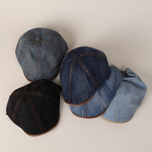 Flat lay of denim flat caps in dark blue, black, and light blue with orange stitching