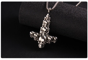 Macro view of punk style silver skull inverted cross pendant on a black textured surface