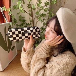 Girl holding a retro black and white checkered corduroy pencil case in a cozy setting