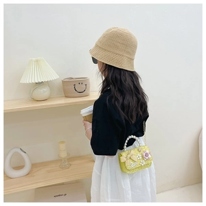 Detail of yellow tweed crossbody bag for kids with pearl handle and bow decoration