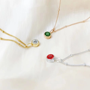 Detail view of three stainless steel birthstone necklaces with green, red and clear crystals.