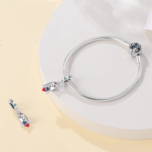 Detail of silver snake chain bracelet featuring a rocket charm with blue stone clasp