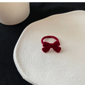 Close-up of a red flocked velvet bow hair tie placed on a white textured ceramic plate