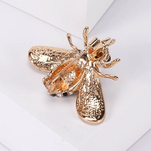 Macro shot of gold metal bee brooch with sparkling crystals and pearl on white display box