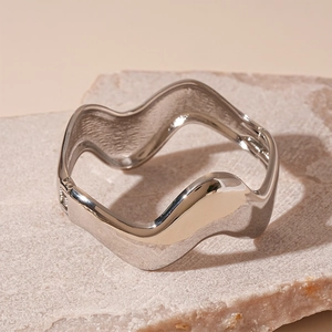 Close-up of a silver wavy metal bangle with mirror finish on natural stone
