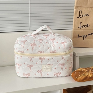 Quilted floral makeup bag with pink bow pattern and handle on a bright minimalist desk