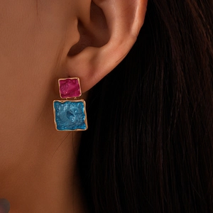 Detail view of geometric square drop earrings with rose red and blue enamel in gold frames
