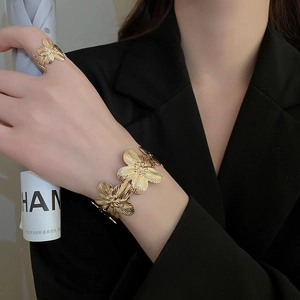 Detail of gold floral textured cuff bracelet and ring set on model wearing black suit