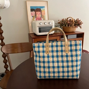 Close-up of blue plaid canvas tote with red floral embroidery and leather handle details