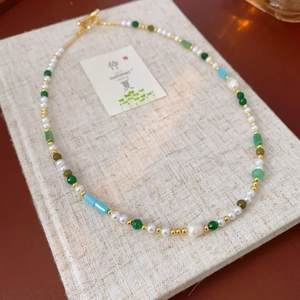 Detail of beaded necklace with freshwater pearls, green gemstones, and golden T-bar clasp