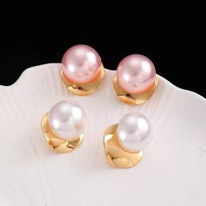 Macro shot of large white and pink pearls set in textured gold C-shaped earrings