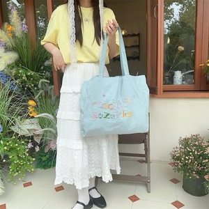 Détail du sac cabas en toile bleu clair avec broderie florale colorée et bandoulière