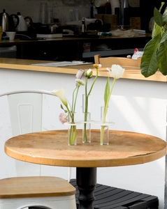 Close-up of three-hole glass test tube vase with tulips on a round wooden table