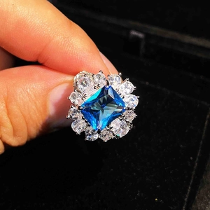Detailed shot of a blue rectangular gemstone ring held in a dark velvet jewelry box