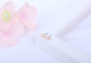 Macro shot of small round pink freshwater pearl earrings on silver studs shown on a white frame