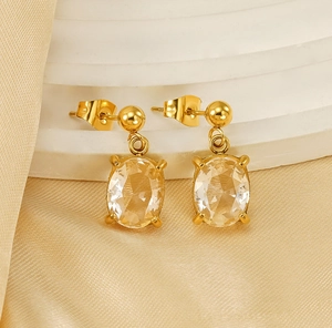 Détail de boucles d'oreilles dorées avec zircone ovale et finition polie sur de la soie