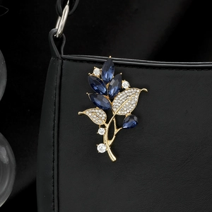 Elegant gold leaf brooch with blue crystals and rhinestones pinned on a black leather bag