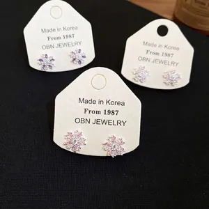 Three pairs of elegant zircon flower stud earrings in purple, white and pink displayed on a card