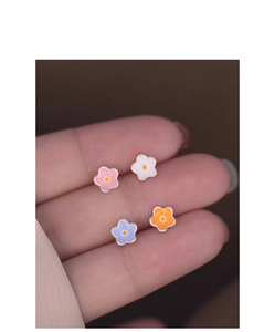 Macro shot of colorful enamel flower earrings on a fingertip showing small size and details