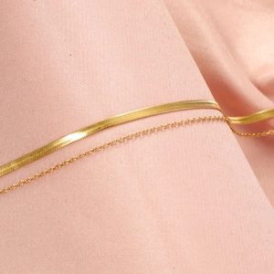Detail of layered gold stainless steel herringbone and cable chain on pink fabric