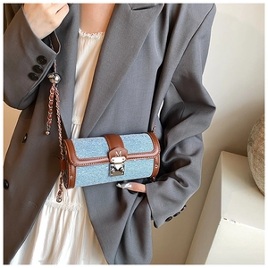 Close-up of a blue denim and brown leather cylinder bag with a silver M buckle and chain