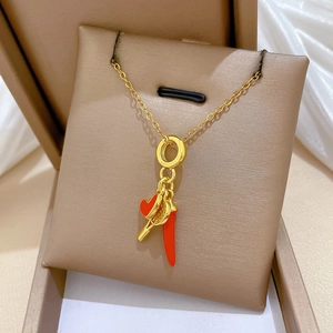 Detail view of gold titanium necklace with red heart key and chili pepper charms