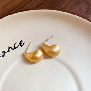Macro shot of matte gold drop earrings on a ceramic tray with fine brushed texture
