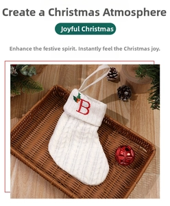 Macro detail of white cable knit Christmas stocking with red embroidered B and holly leaves