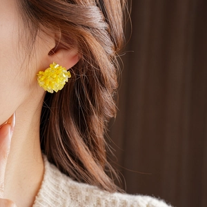 Detail of yellow beaded flower cluster stud earring worn by a model with brown curly hair