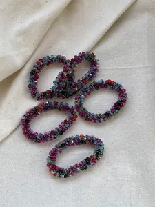 Close-up of colorful crystal beaded hair ties on a cream textured linen background