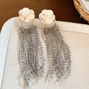 Close-up of elegant flower stud earrings with grey beaded fringe on a textured tray