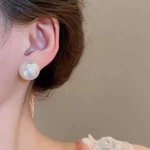 Macro shot of large high-luster pearl stud earring with mirror-like surface on model ear