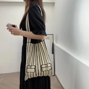 Detail of knitted pleated tote bag with black stripes and decorative pockets on cream base