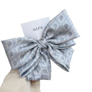Hand holding a large triple-layered light blue floral silk bow hair clip with brand tag