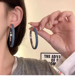 Close-up of oversized denim hoop earrings with blue fabric wrapping and silver metal inner