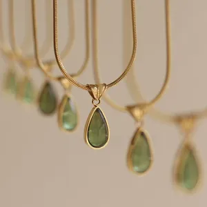 Close-up of translucent green water drop pendants with golden snake chains in a row