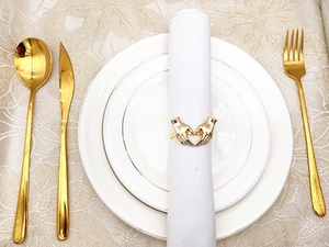 Macro shot of gold heart napkin ring on a white napkin with luxury golden cutlery