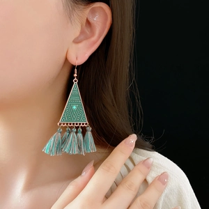 Detailed view of bohemian triangle earrings with green tassels worn by a model