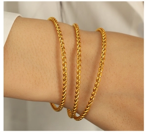 Detail of three stacked gold twisted rope bangles on model's wrist with high metallic shine